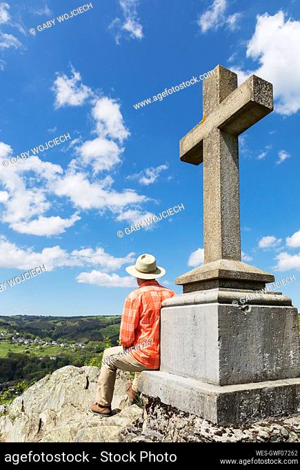 Man sitting by Summit Cross on sunny day, Simmerath, Eifel, North Rhine Westphalia, Germany