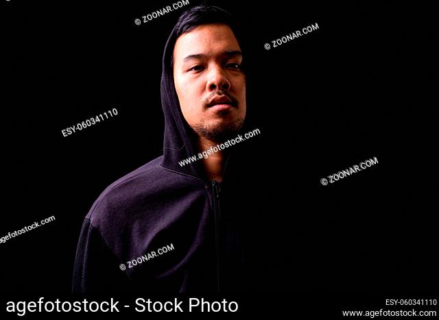 Studio shot of young Asian man wearing hoodie against black background