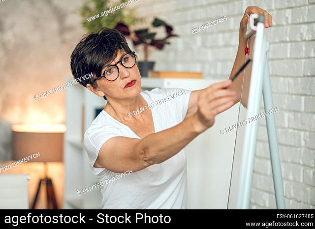 Working on project. Mature dark-haired woman standing near the flipchart and working on project details