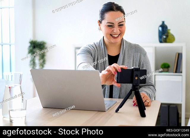 Happy businesswoman adjusting smart phone on tripod during video call at home