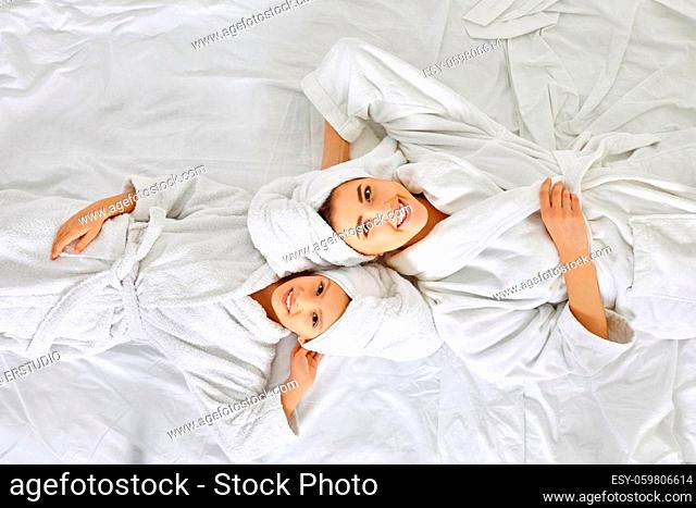 happy mom and daughter in white bathrobe lie on the bed in the bedroom, Top view