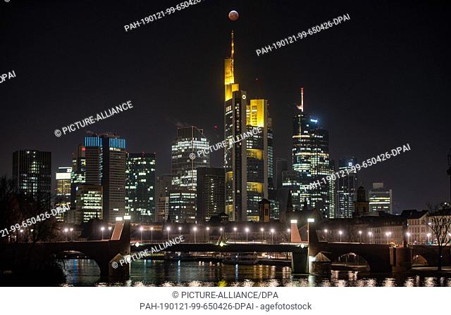 21 January 2019, Hessen, Frankfurt/Main: As a red, so-called ""blood moon"", the full moon stands above the Frankfurt skyscrapers and the Commerbank (M)...