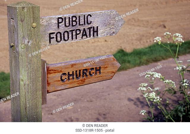 UK, England, Norfolk, Detail of wooden signpost with two directional signs stating Public Footpath and Church with track tilled field and Cow parsley