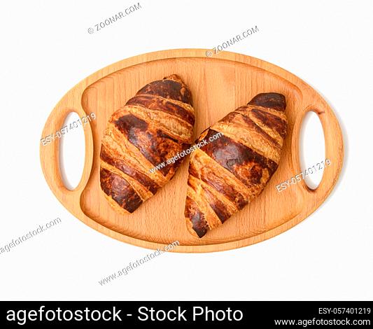 two baked croissants lie on a wooden tray, food isolated on white background, top view