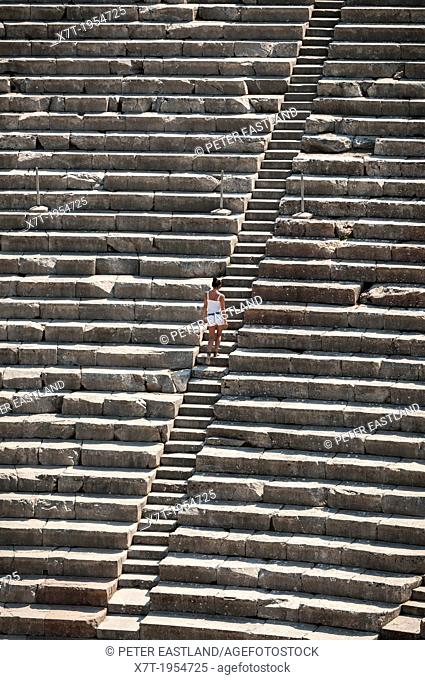 A woman climbs steps amongst the tierd seating of the Classical Greek theatre at Ancient Epidaurus, Argolid, Peloponnese, Greece