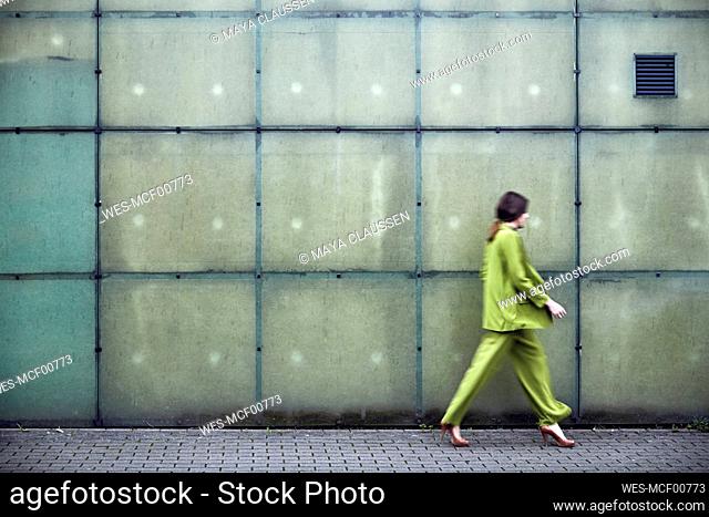 Businesswoman wearing green suit passing a wall