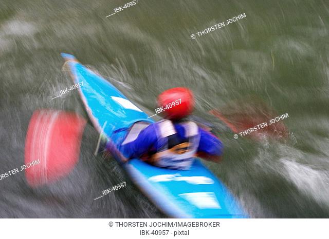 Blured picture of an fast kajakdriver with red helmet an blue boat ( Isar , munich)