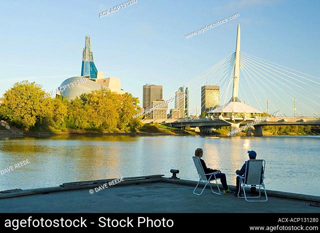 couple relaxing , Winnipeg skyline from St. Boniface showing the Red River, Esplanade Riel Bridge and Canadian Museum for Human Rights, Manitoba, Canada