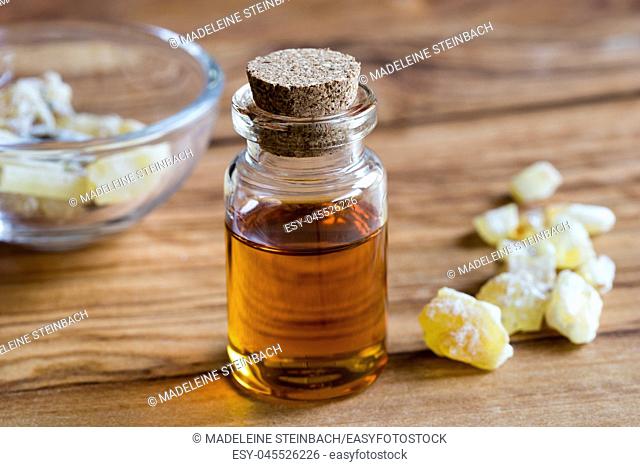 A bottle of frankincense essential oil with frankincense resin crystals in the background, on a wooden table