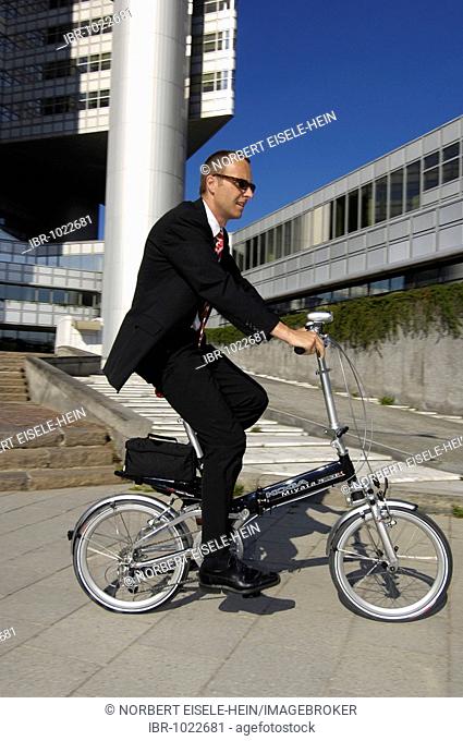Businessman on his way to work on a folding bike, Hypobank building, Bogenhausen, Munich, Bavaria, Germany, Europe