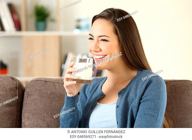 Happy woman holding a glass of milk sitting on a couch in the living room at home