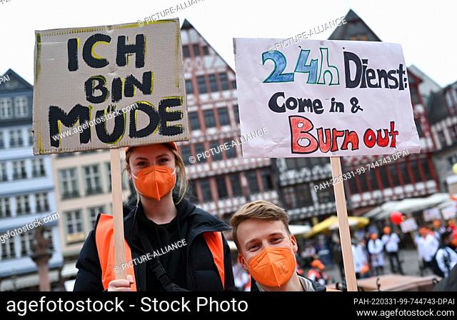 31 March 2022, Hessen, Frankfurt/Main: Two demonstrators hold placards reading ""I'm tired"" and ""24h service: Come in & Burn out"" at the central rally of the...