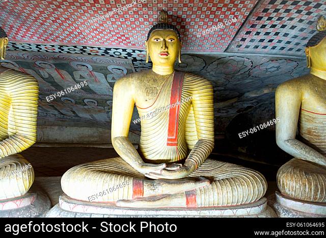Group of sitting Buddha statues in cave buddhist temple with bright painted murals on walls and ceiling in Dambulla Golden temple in Sri Lanka