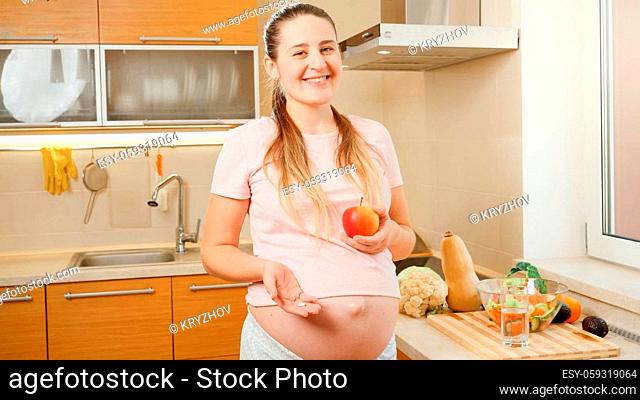 SMiling young pregnant woman holding vitamin pill and fresh ripe apple in hands. Concept of healthy lifestyle, nutrition and hydration during pregnancy