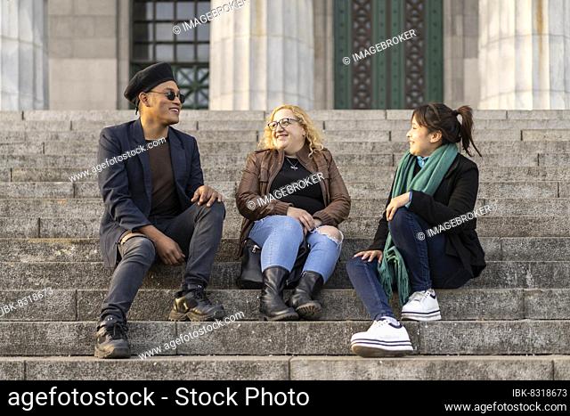 Multi ethnic group of friends sitting on some stairs having a good time chatting and laughing