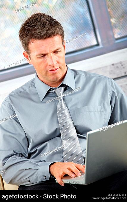 Smart businessman with laptop in lap typing on keyboard concentrating looking at screen