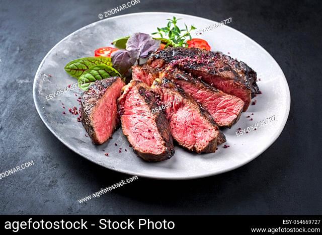 Barbecue dry aged wagyu entrecote beef steak with lettuce and tomatoes as closeup on a modern design plate