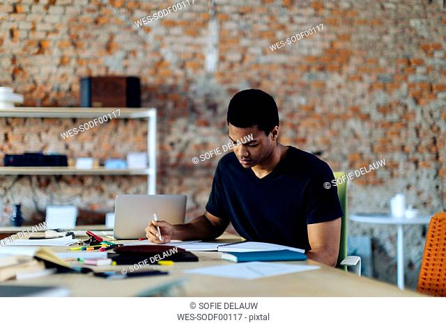 Young man sitting at table taking notes
