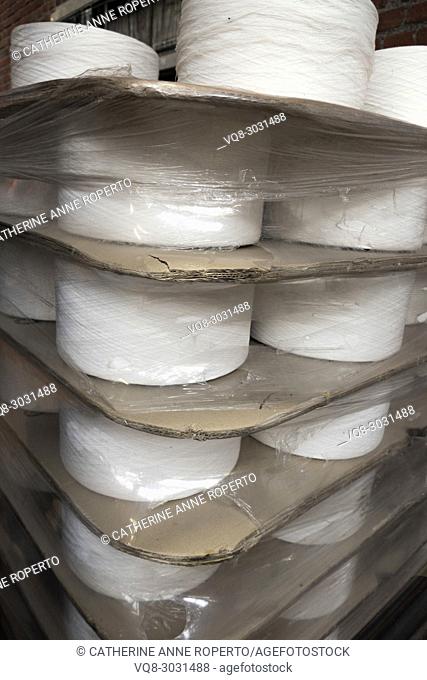 Confrontational flat industrial spools of white thread packaged with layers of thick corrugated card dividers and shrink wrapped in reflective polythene for the...
