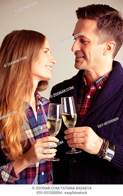 Happy mature couple in casual clothes embracing and clinking glasses of champagne