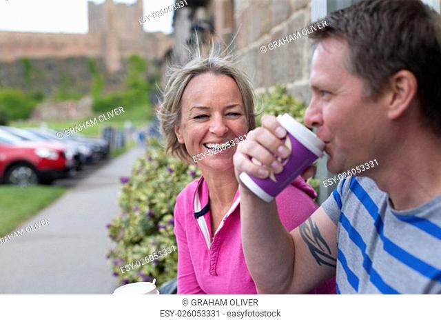 Mature couple laughing as they sit and enjoy a hot drink from a takeaway cup. They are wearing casual clothing and look very happy