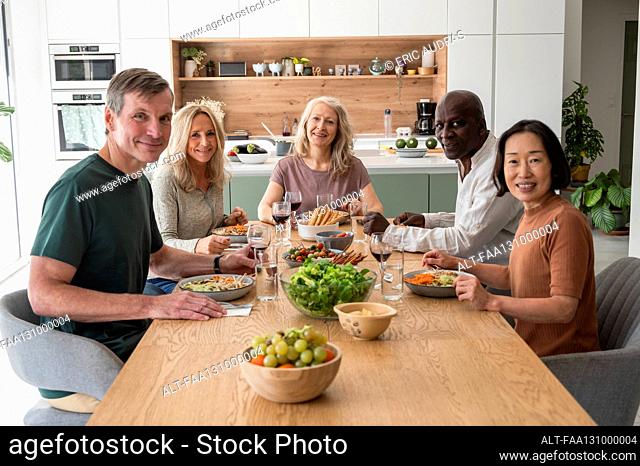 Group of diverse senior friends gathered together for lunch in the kitchen