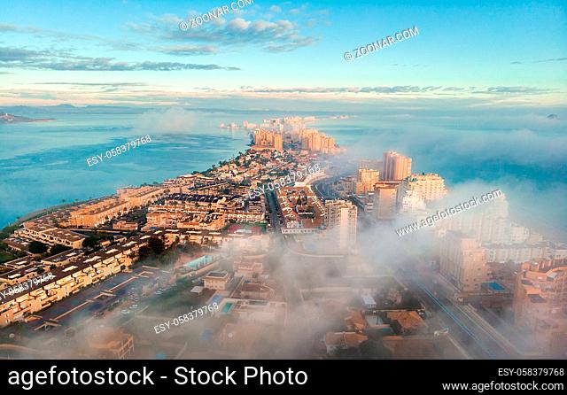 Aerial drone point of view La Manga del Mar Menor cityscape and Mediterranean sea during sunrise, cloudy misty sky, picturesque scenery