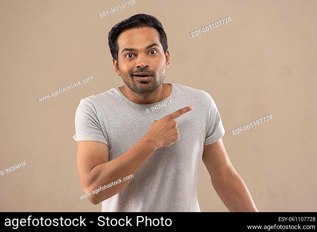 Portrait of a surprised young man pointing away with his finger