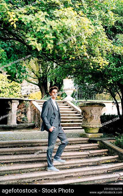 Serious groom stands with his hand in his pocket on the stairs in the park. Lake Como. High quality photo