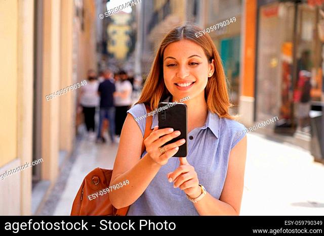 Portrait of smiling young woman walking using a smartphone in the street