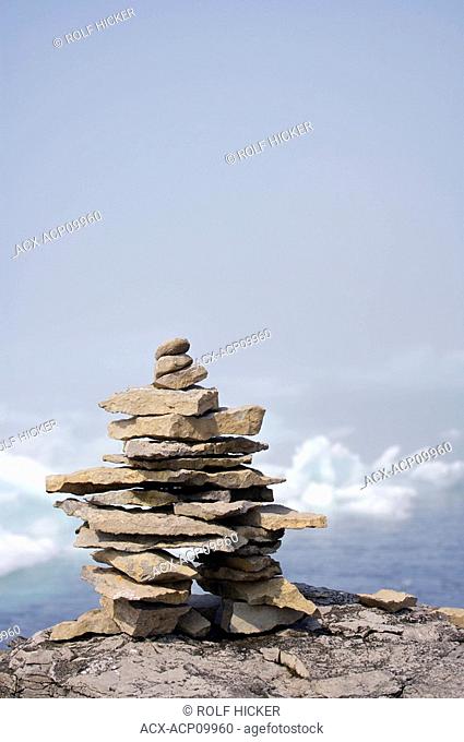 Rock inukshuk on a ledge backdropped by pack ice veiled by fog in the Strait of Belle Isle, Labrador Coastal Drive, Viking Trail, Southern Labrador