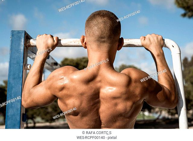 Rear view of barechested muscular man practicing fitness exercises on football goal outdoors