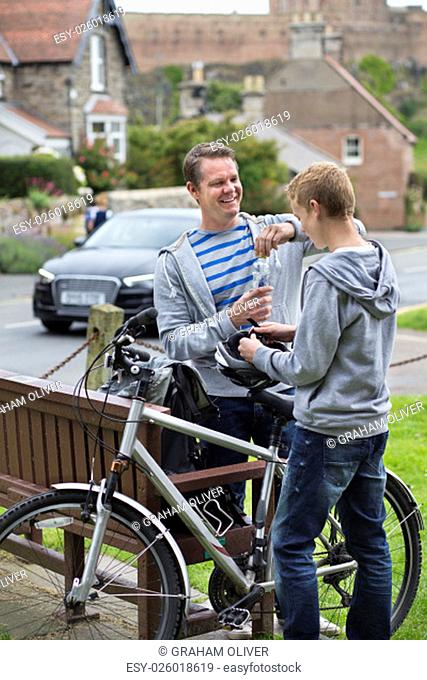 Father and Son stopping in a village in the middle of their bike ride to take a drink. They are wearing casual clothing and smiling