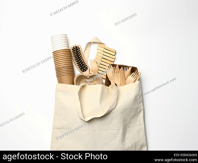 white textile bag and disposable tableware from brown craft paper on a white background. View from above, plastic rejection concept, zero waste
