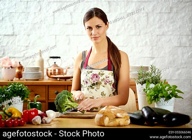 beautiful young woman, brunette cutting broccoli in the kitchen on a table full of organic vegetables