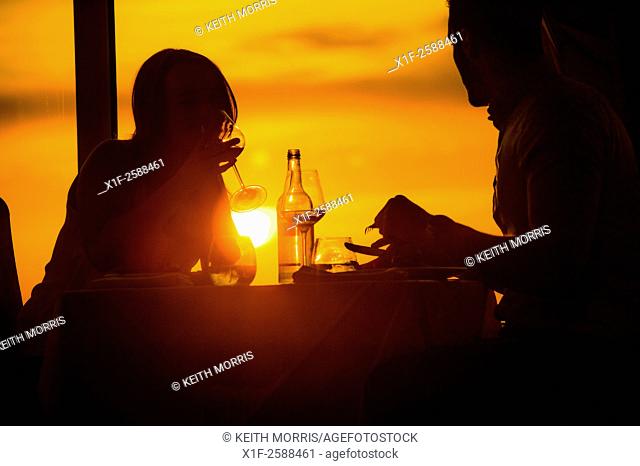 Romantic meal: A couple, man, woman eating a meal and drinking wine in a hotel restauraunt at sunset UK