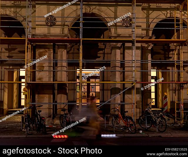A cyclist drives past an old building in Berlin in the dark
