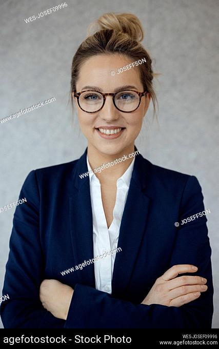 Smiling beautiful businesswoman with arms crossed against gray background