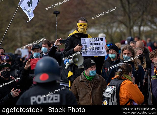 13 April 2021, Berlin: A masked demonstrator stands in front of a police officer in the government quarter and protests with other people against the tightening...