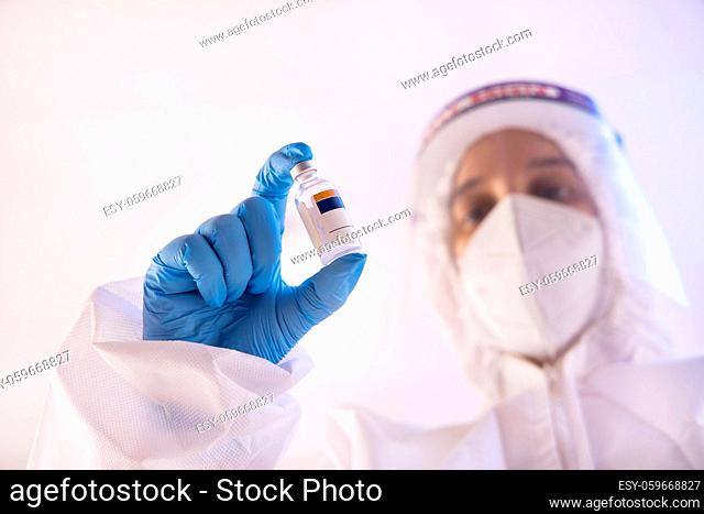 A doctor in PPE kit holding a bottle of covid vaccine in hand