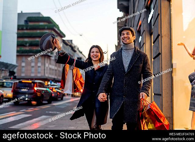 Happy girlfriend and boyfriend holding hands while walking together in city