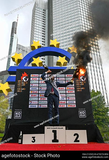 05 May 2021, Hessen, Frankfurt/Main: A member of the activist group ""KoalaKollektiv"" holds a burning cup in front of the Euro sculpture in Frankfurt's banking...