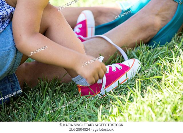 Caucasian Little toddler girl with blue free playing on her mom's lap on the grass and tiing her mini converse pink shoe
