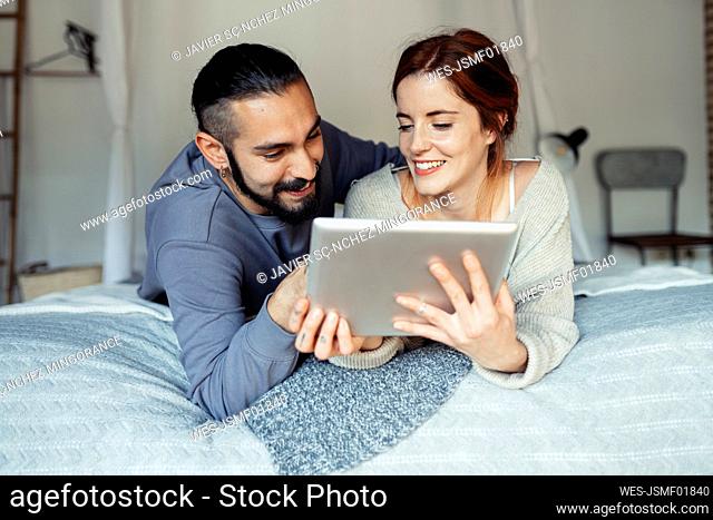 Smiling couple using digital tablet while lying on bed at home
