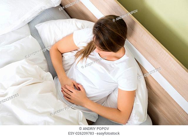 Young Woman With Stomach Ache Lying On Bed In Her Room