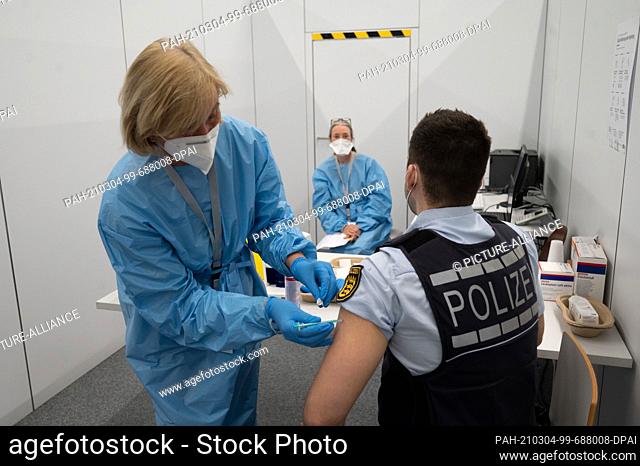 04 March 2021, Baden-Wuerttemberg, Heilbronn: A police officer (r) is vaccinated with AstraZeneca's Corona vaccine by vaccination staff at the Kreisimpfzentrum...