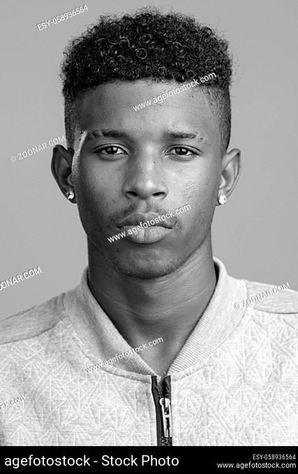 Studio shot of young handsome African man with Afro hair isolated against white background in black and white