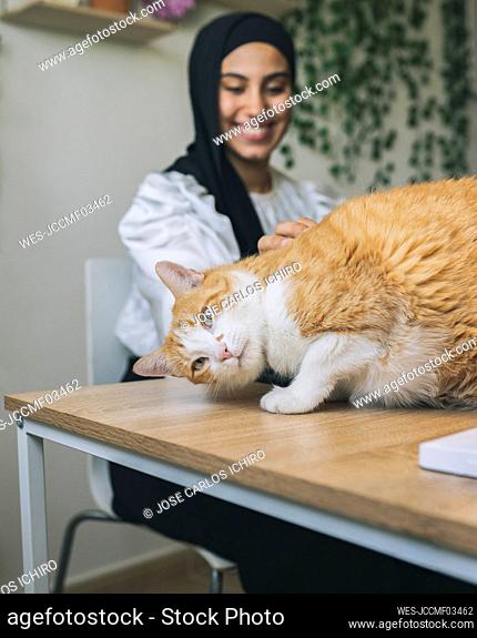 Smiling female professional stroking ginger cat at home