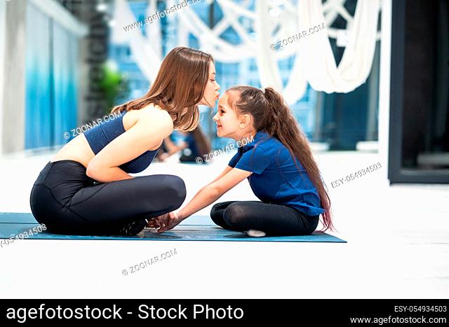 Young adult mother and little daughter together practicing yoga in the gym