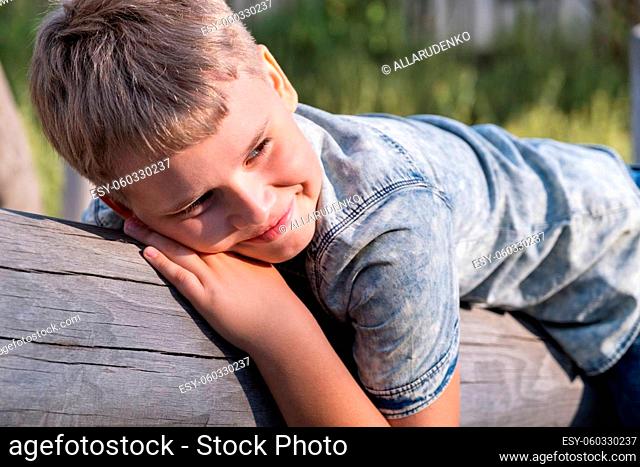 Cute blond boy the boy lies on a wooden beam on playground in a public park